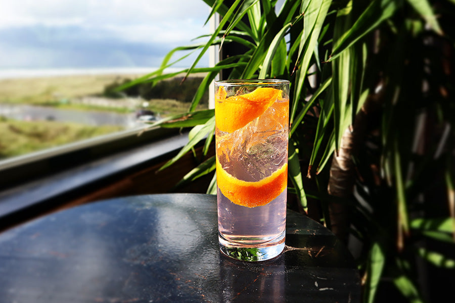 Cocktail with orange slices in a glass on a reflective surface with a scenic background